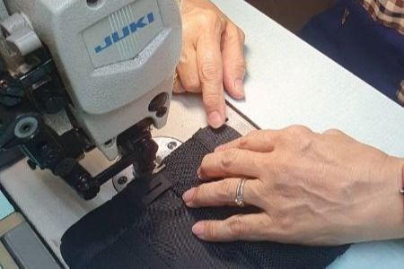Technician using an industrial sewing machine to stitch black fabric, illustrating R&D precision and hands-on evaluation in transforming custom designs to manufacturable solutions